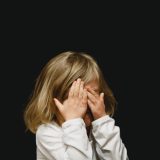 Dziecko zakrywające twarz rękami na czarnym tle