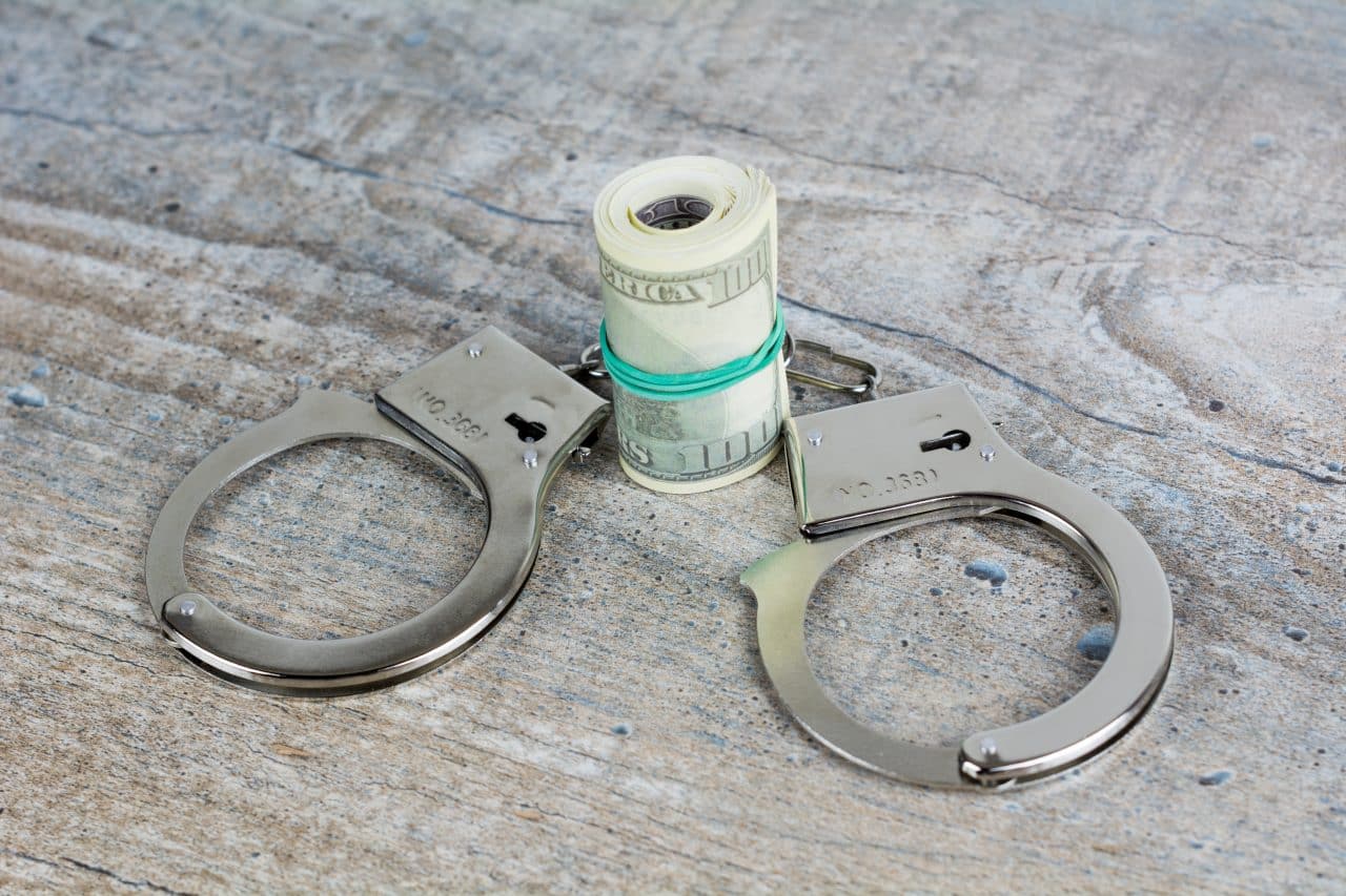 kajdanki i plik banknotów leżące na szarym blacie - adwokat opole sprawy karne